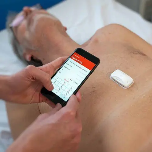 Healthcare professional uses smartphone to monitor patient's health via chest sensor in medical setting.