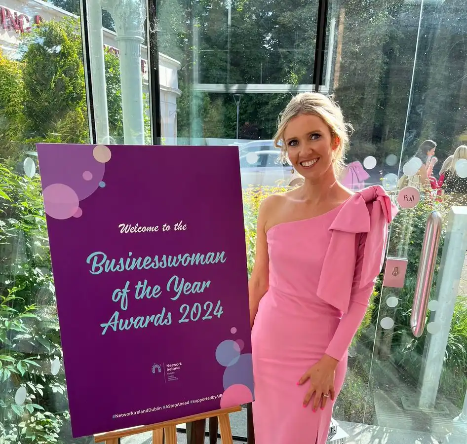 Woman in pink dress at Businesswoman of the Year Awards 2024 next to purple welcome sign.